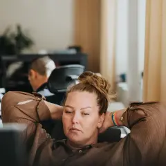 A woman with her hands behind her head, looking tired at her desk. This image captures the essence of presenteeism, where someone is physically at work but not fully engaged or productive.