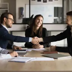 Successful business meeting where two men shake hands, showcasing their influencing and negotiation skills. Two women smile, observing the agreement.