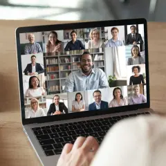 A person's hands on a laptop keyboard, viewing a virtual networking event with multiple participants on screen. This image illustrates how to host a virtual networking event.