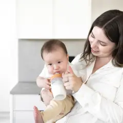 A mother smiles as she feeds her baby a bottle, a sweet moment before going back to work after maternity leave.