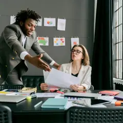 A man in a suit gestures emphatically during a difficult conversations training session with a woman at a desk.