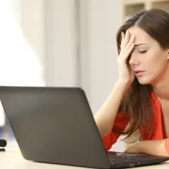 A woman with her hand on her forehead, looking stressed at her laptop, likely after being passed over for promotion.