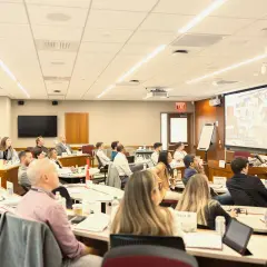 Attendees at negotiation seminars listen intently to a speaker presenting on a large screen.