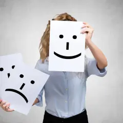 A person holds a happy face, while another sad face is shown. This could represent people who complain all the time, hiding their true feelings.