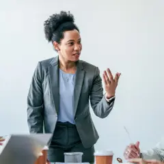 A diverse team engages in a communications leadership development program, with a woman in a grey suit leading the discussion.