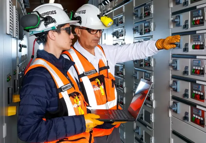 Two engineers in a control room, one pointing at a panel, the other holding a laptop, showcasing the characteristics of innovation in electrical systems.