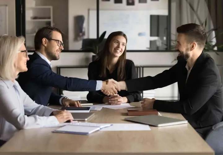 Successful business meeting where two men shake hands, showcasing their influencing and negotiation skills. Two women smile, observing the agreement.