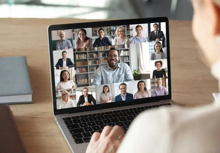 A person's hands on a laptop keyboard, viewing a virtual networking event with multiple participants on screen. This image illustrates how to host a virtual networking event.