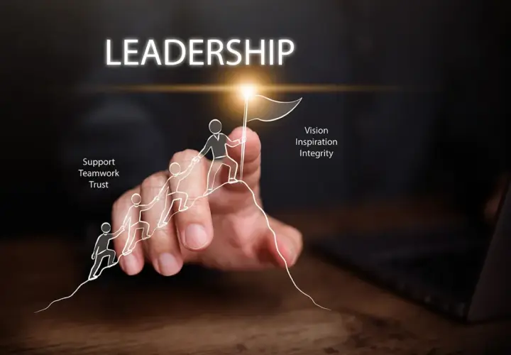 A hand guides a drawn team up a mountain, symbolizing leadership development. Key traits like vision, inspiration, integrity, support, teamwork, and trust are highlighted.