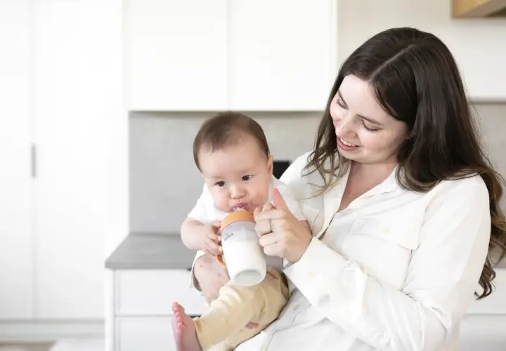 A mother smiles as she feeds her baby a bottle, a sweet moment before going back to work after maternity leave.
