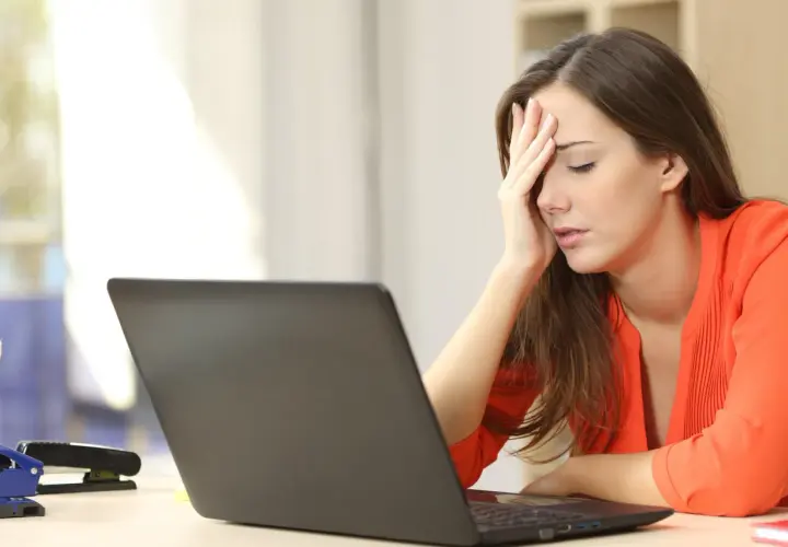 A woman with her hand on her forehead, looking stressed at her laptop, likely after being passed over for promotion.