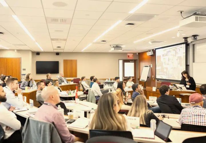 Attendees at negotiation seminars listen intently to a speaker presenting on a large screen.