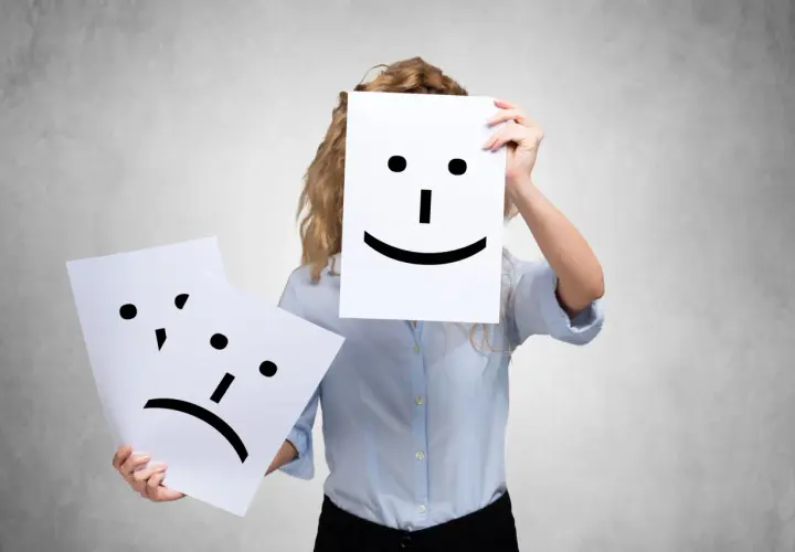 A person holds a happy face, while another sad face is shown. This could represent people who complain all the time, hiding their true feelings.