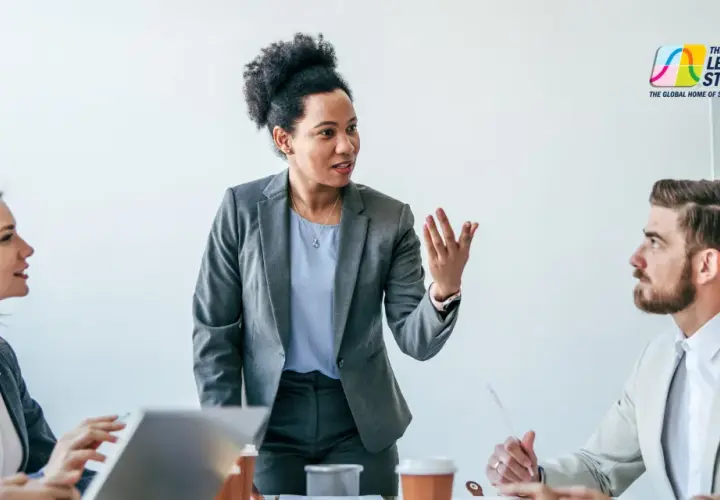 A diverse team engages in a communications leadership development program, with a woman in a grey suit leading the discussion.
