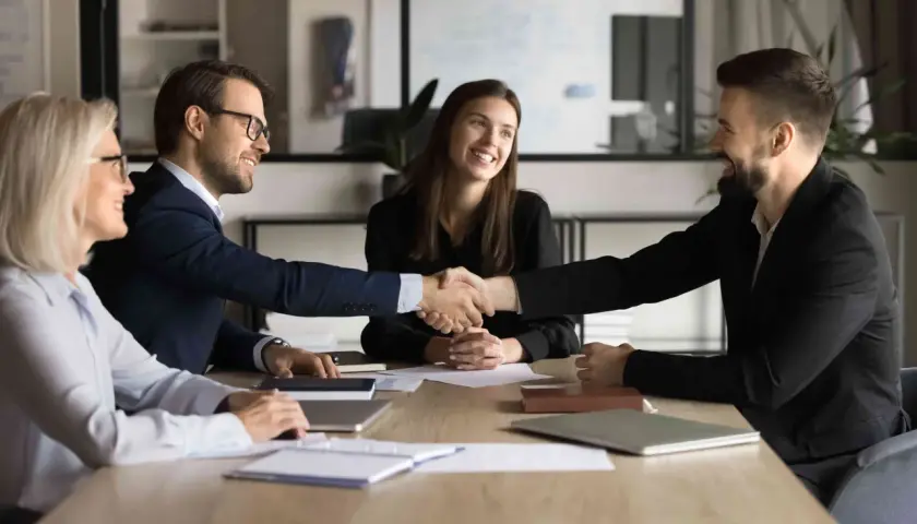 Successful business meeting where two men shake hands, showcasing their influencing and negotiation skills. Two women smile, observing the agreement.