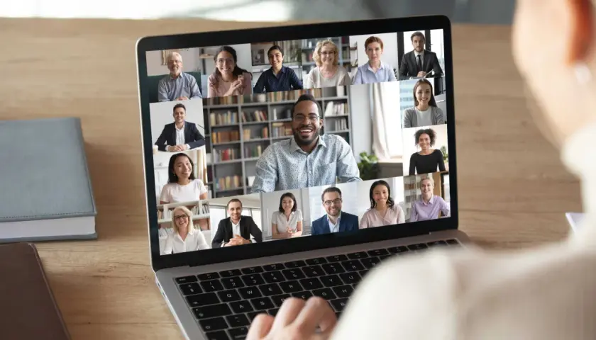 A person's hands on a laptop keyboard, viewing a virtual networking event with multiple participants on screen. This image illustrates how to host a virtual networking event.