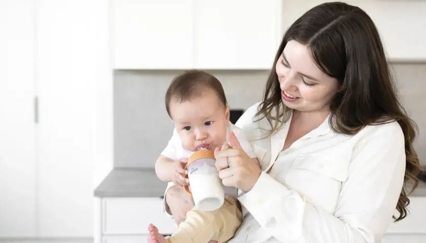 A mother smiles as she feeds her baby a bottle, a sweet moment before going back to work after maternity leave.