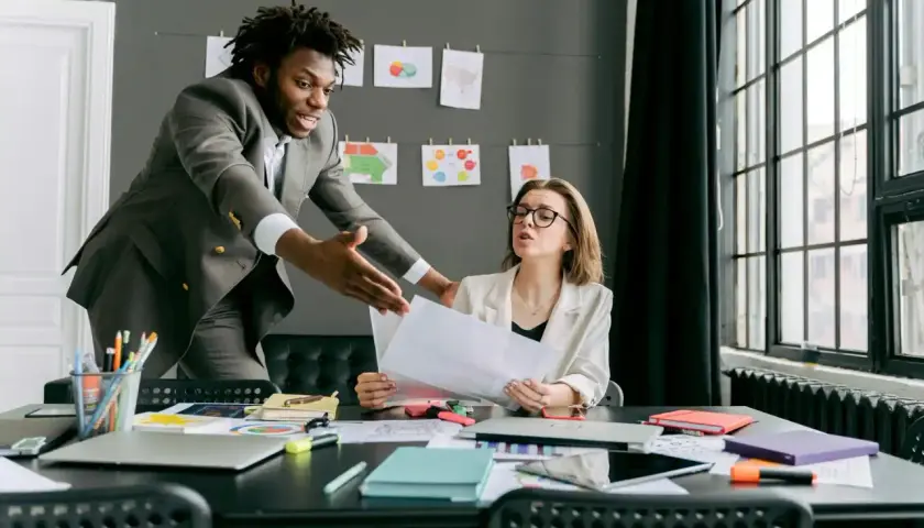 A man in a suit gestures emphatically during a difficult conversations training session with a woman at a desk.