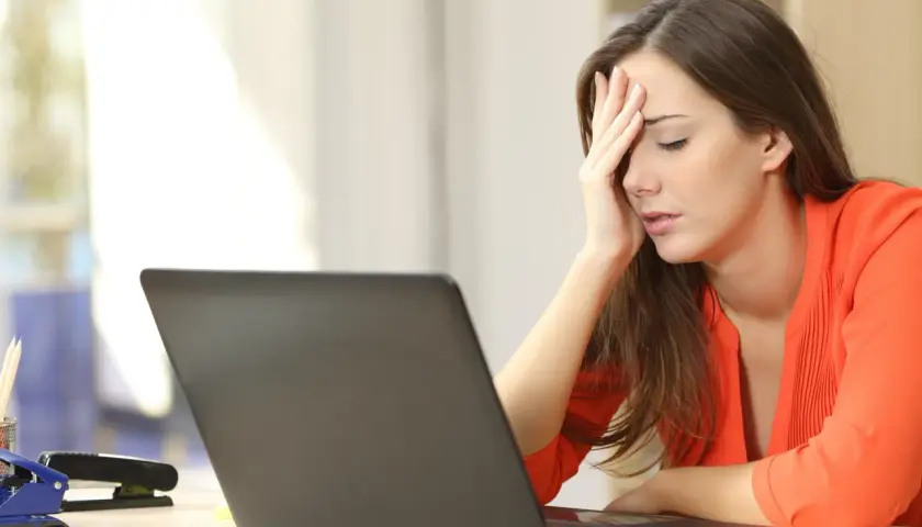A woman with her hand on her forehead, looking stressed at her laptop, likely after being passed over for promotion.