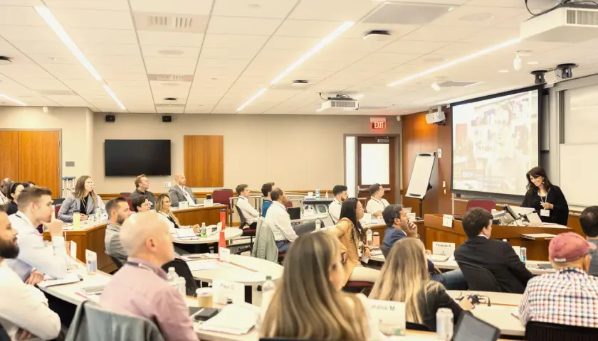 Attendees at negotiation seminars listen intently to a speaker presenting on a large screen.