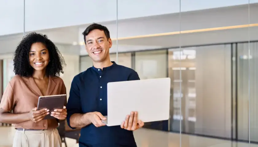 Smiling colleagues with a laptop and tablet, ready for their next step in the leadership development program.