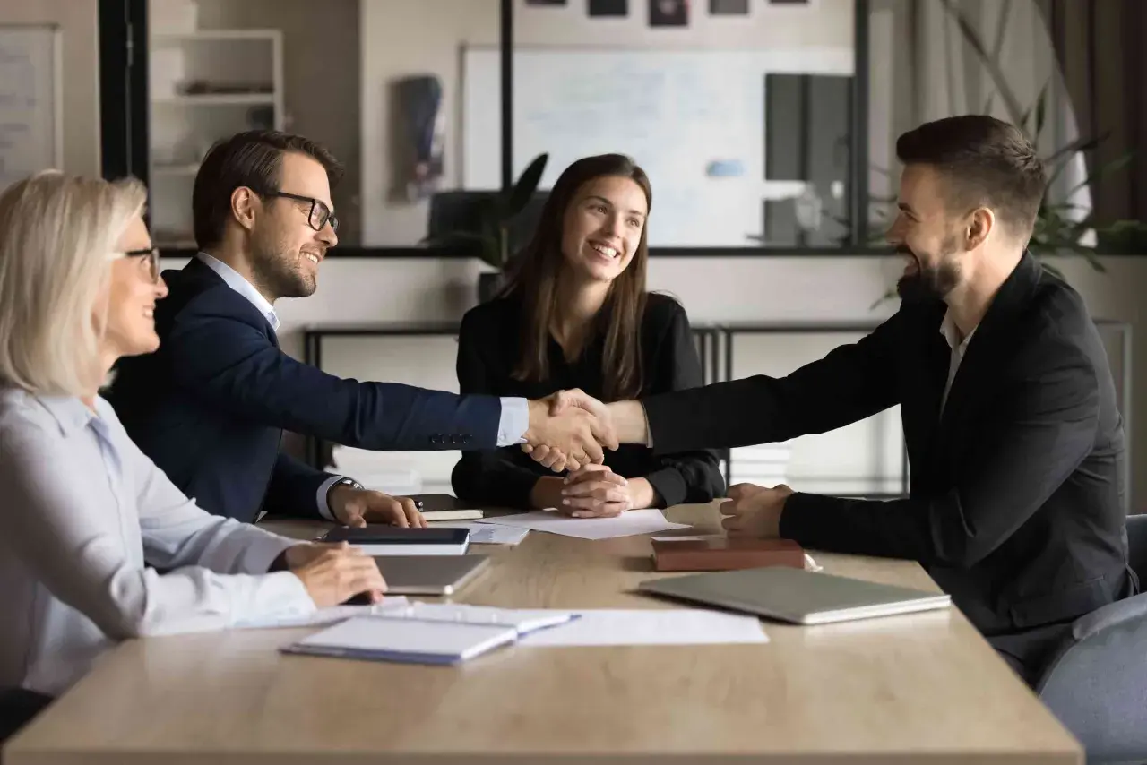 Successful business meeting where two men shake hands, showcasing their influencing and negotiation skills. Two women smile, observing the agreement.