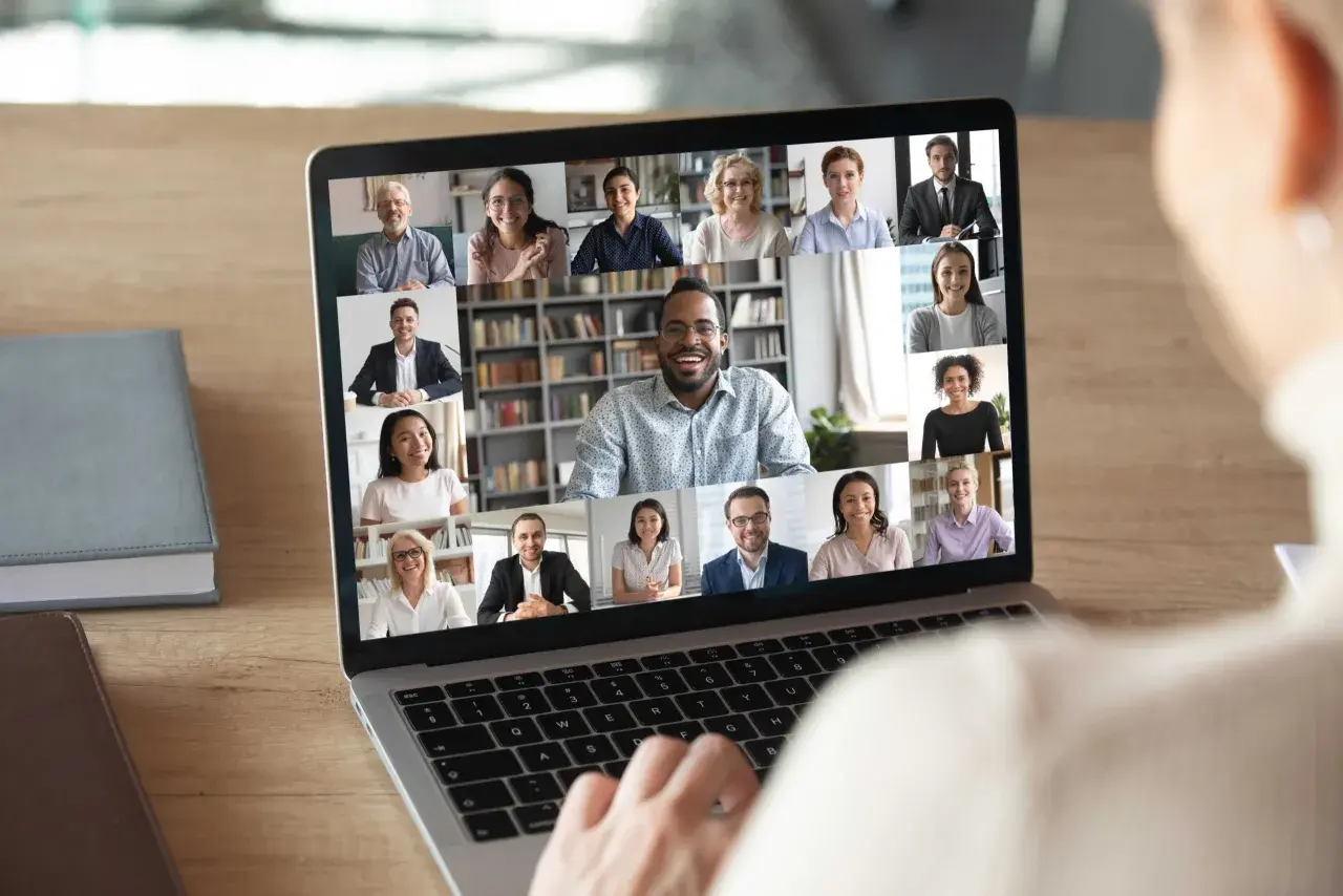 A person's hands on a laptop keyboard, viewing a virtual networking event with multiple participants on screen. This image illustrates how to host a virtual networking event.