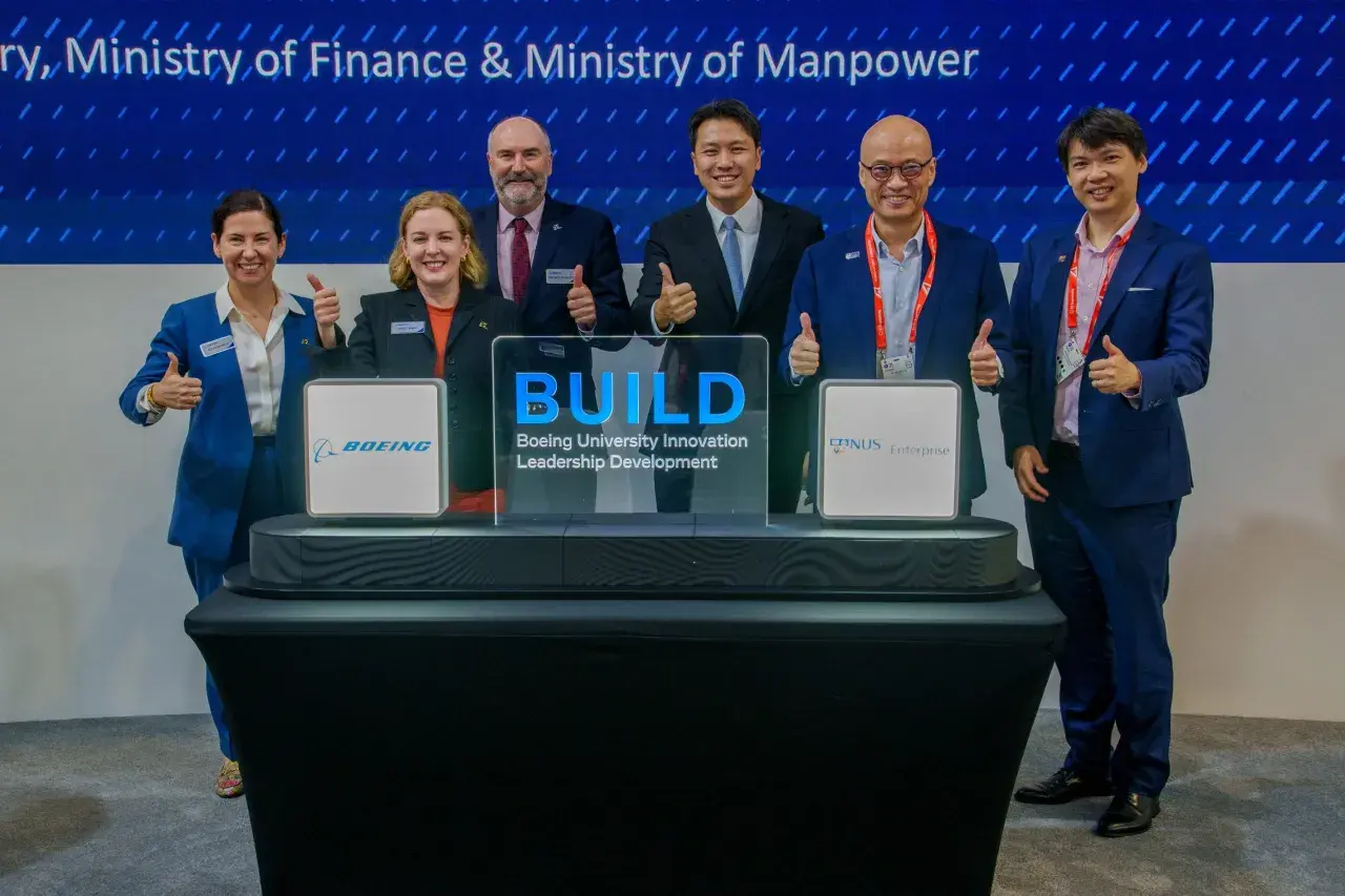 Six individuals in suits give thumbs up at a ceremony for Boeing University Innovation Leadership Development.