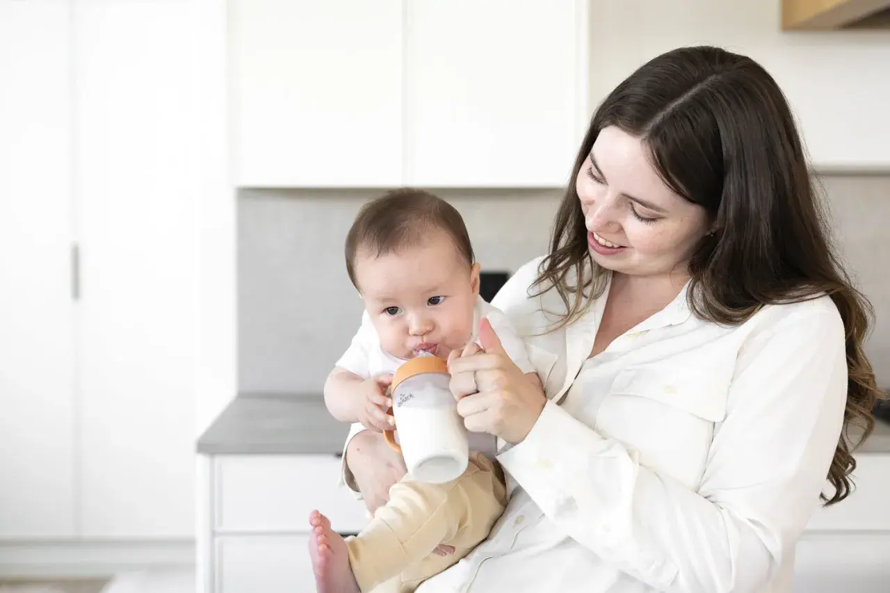 A mother smiles as she feeds her baby a bottle, a sweet moment before going back to work after maternity leave.