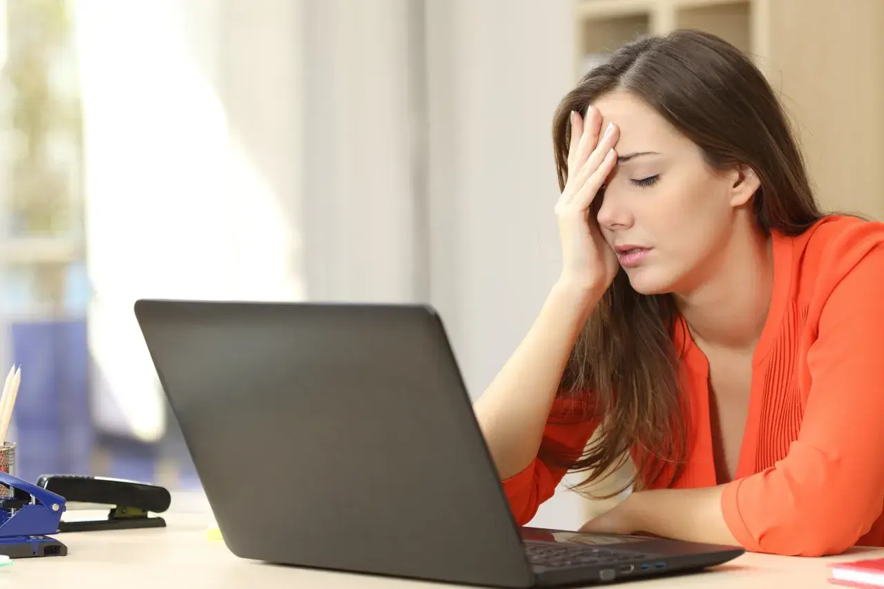 A woman with her hand on her forehead, looking stressed at her laptop, likely after being passed over for promotion.