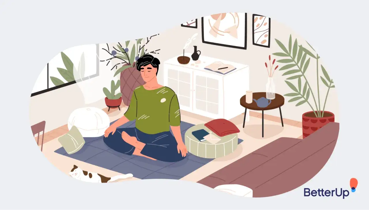 A man meditates in a cozy room, finding peace and job security amidst plants and a sleeping cat.