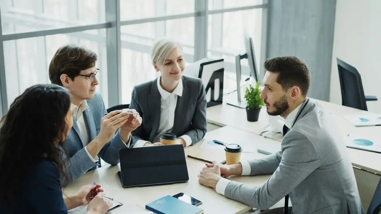 A diverse team discusses evolving workforce trends around a table, with a tablet and coffee cups present.