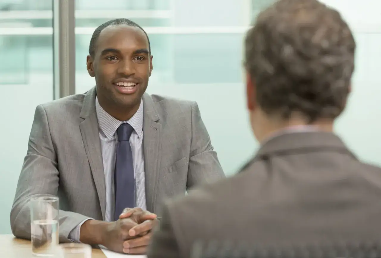 A man in a suit smiles, hands clasped, as he prepares to tell his boss he's quitting.
