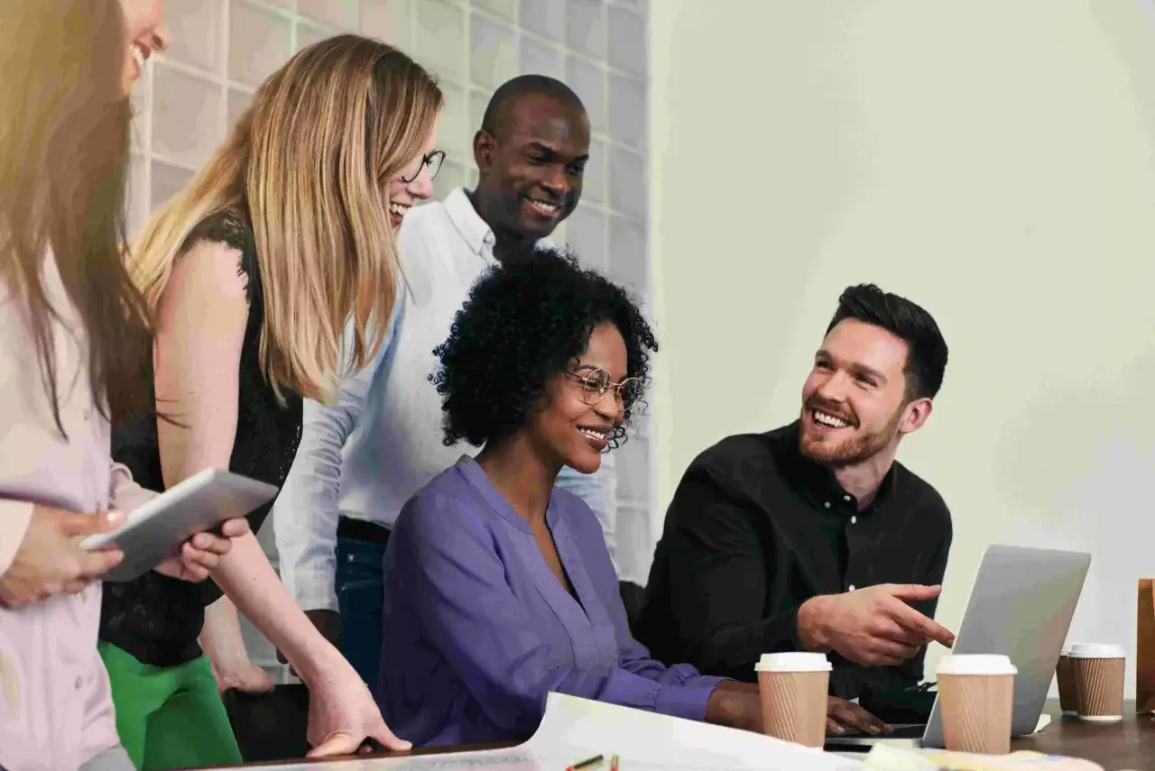 A diverse team collaborates, showcasing a customer centric culture as they brainstorm solutions around a laptop.