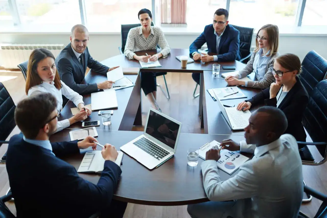 A diverse team collaborates, discussing how to handle a crisis situation. They are gathered around a table with laptops and documents.