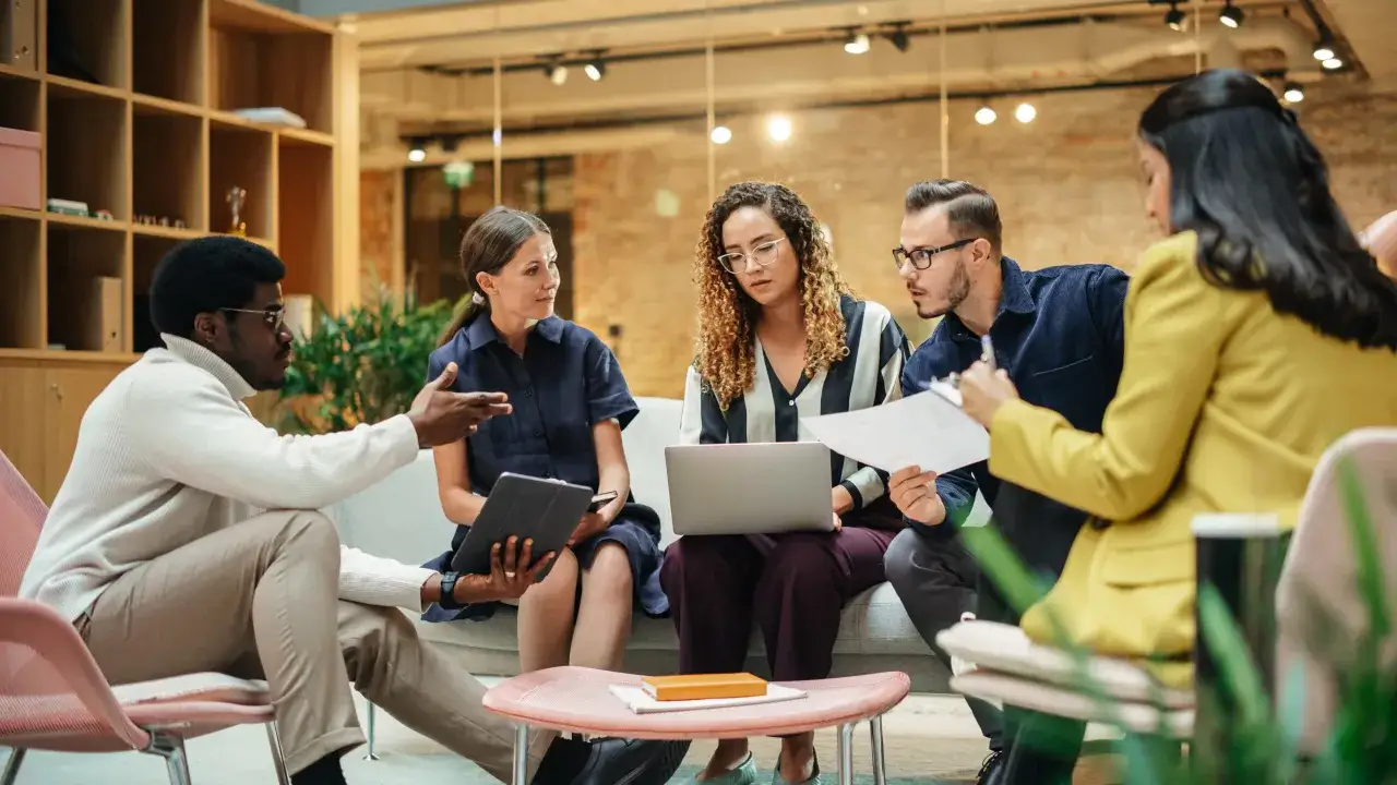 A diverse group collaborates, discussing ideas. This scene illustrates how to be a good mentor by fostering teamwork and sharing knowledge.