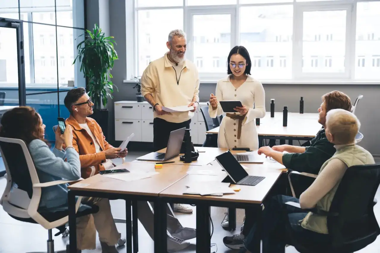 A team engages in corporate digital training, with a presenter using a tablet and a colleague holding papers.