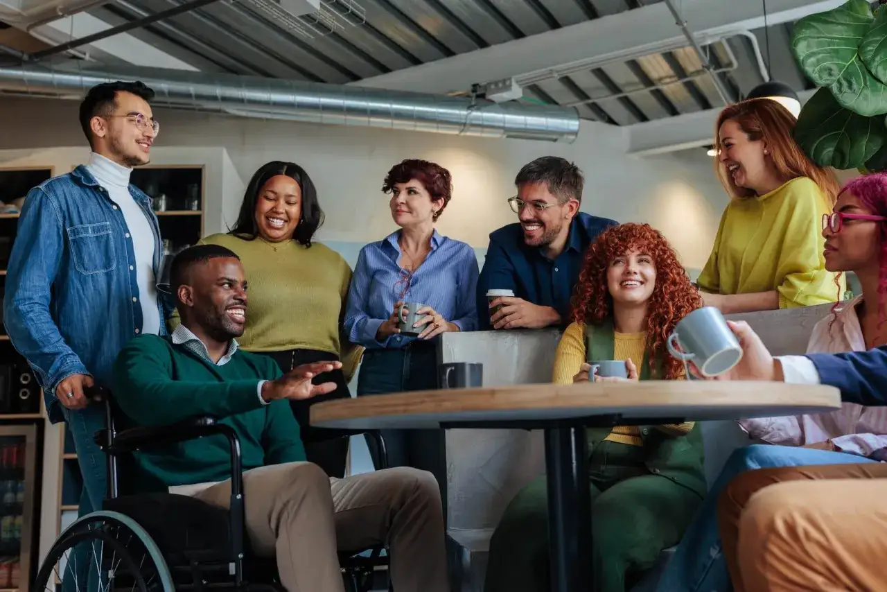 A diverse group of colleagues, including someone in a wheelchair, share smiles and coffee, embodying the spirit of building a coaching culture.