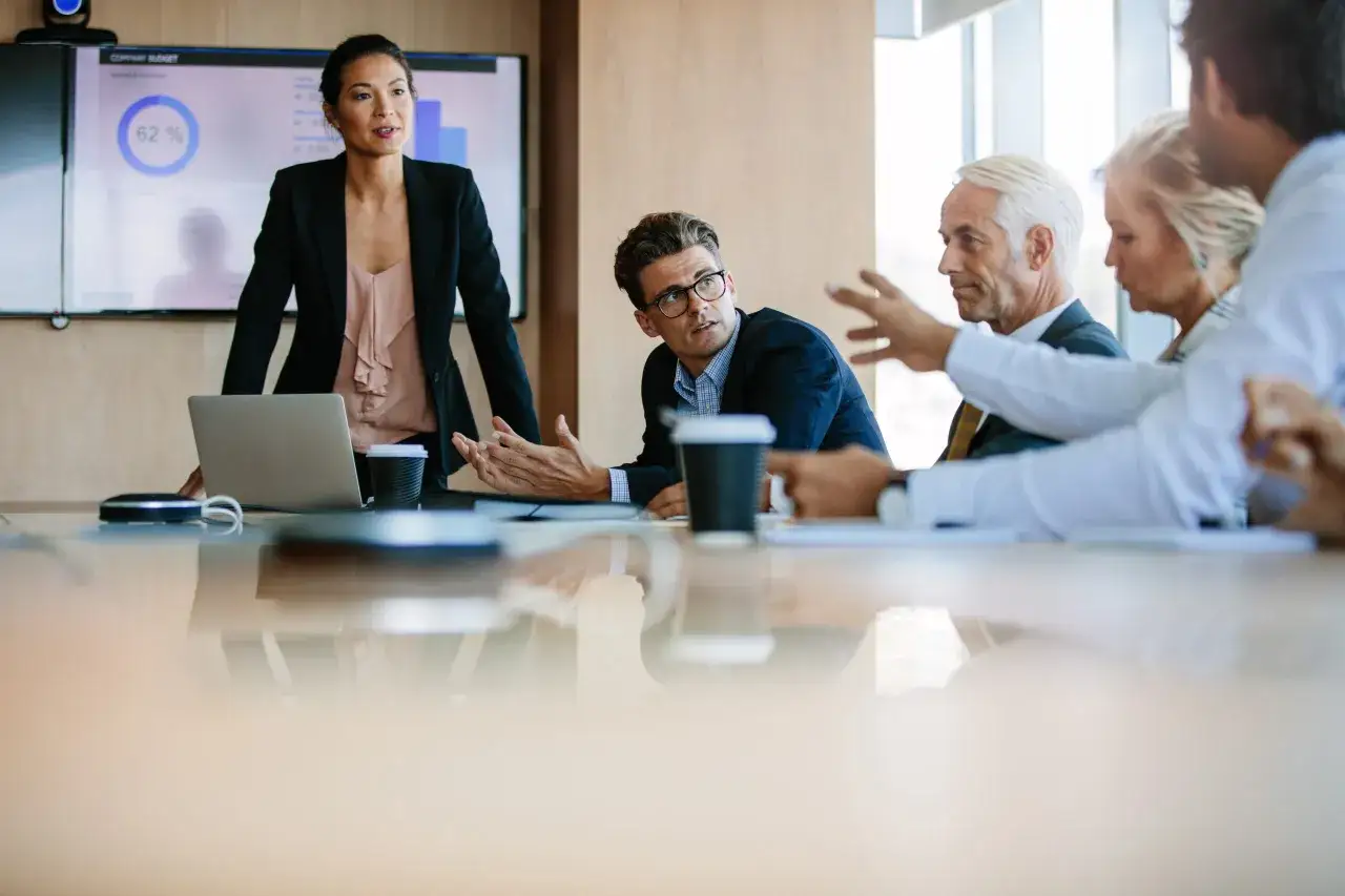 A diverse team discusses how to use AI responsibly, with a woman presenting data on a screen and colleagues engaged in conversation.