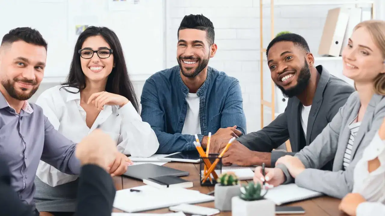 A diverse team smiles and collaborates around a table, navigating change with optimism and shared purpose.