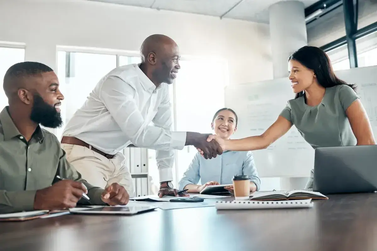 A successful handshake seals a deal after negotiation classes. Three colleagues smile in a bright office setting.