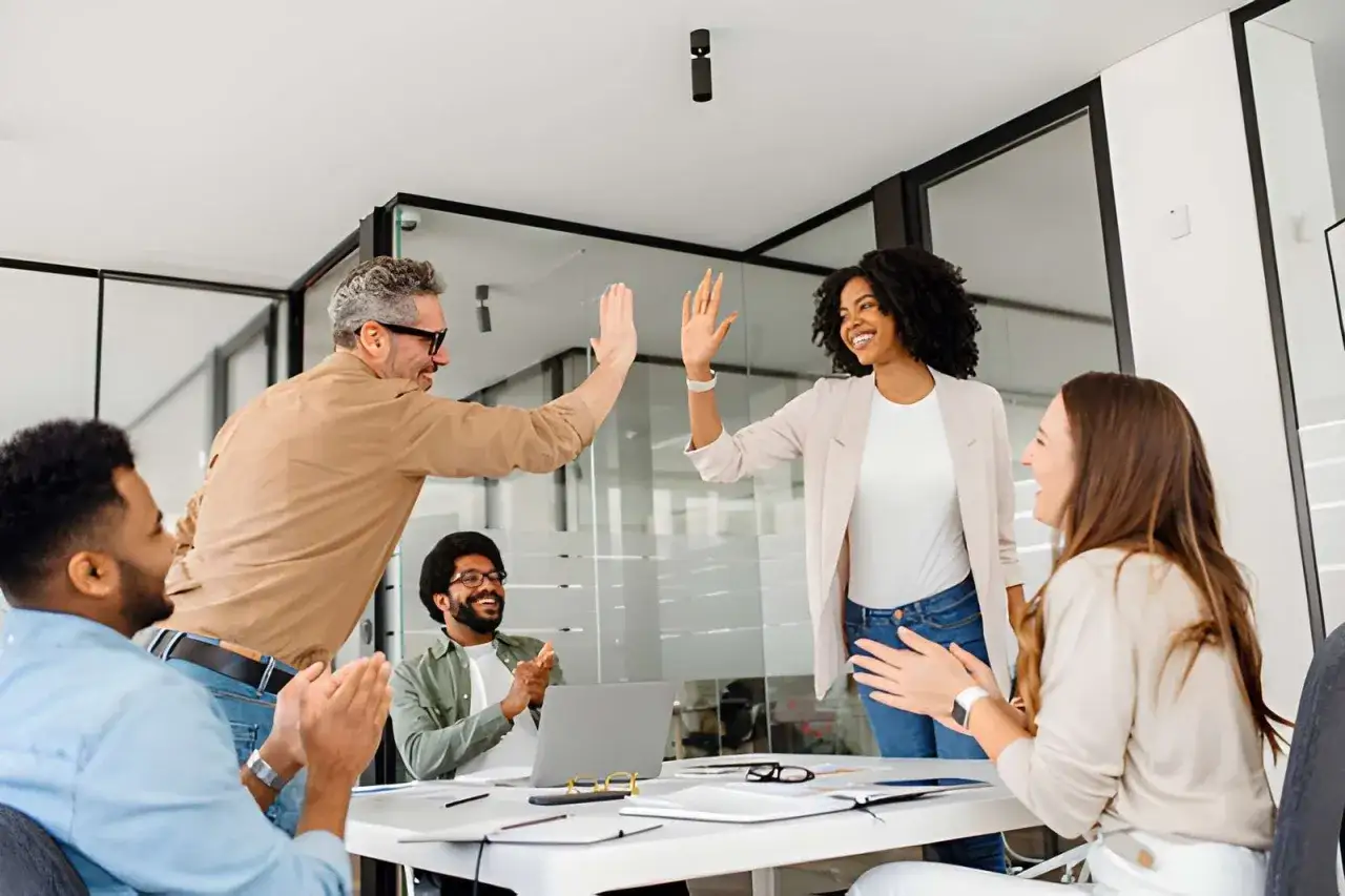 A diverse team celebrates success with high-fives, showcasing effective leadership communication and collaboration in a modern office setting.