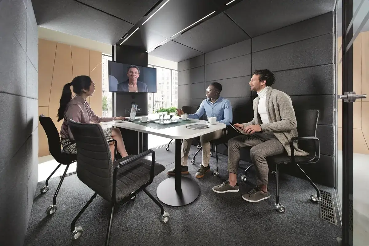 Three colleagues in a modern meeting room discuss important questions to ask your new boss, with a fourth person appearing on a screen.