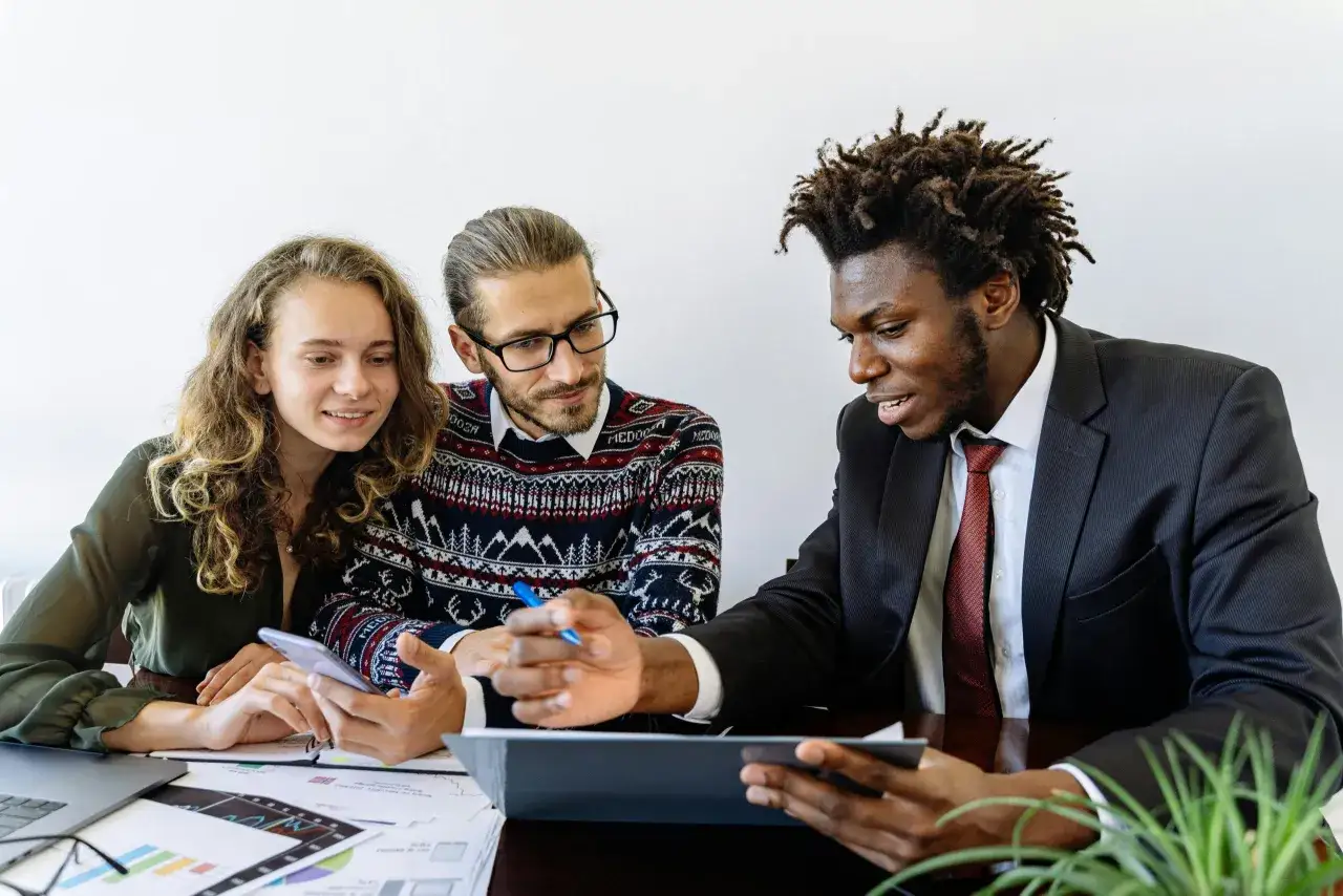 A diverse team discusses a deal, with one man pointing at a tablet, illustrating learning negotiation skills.