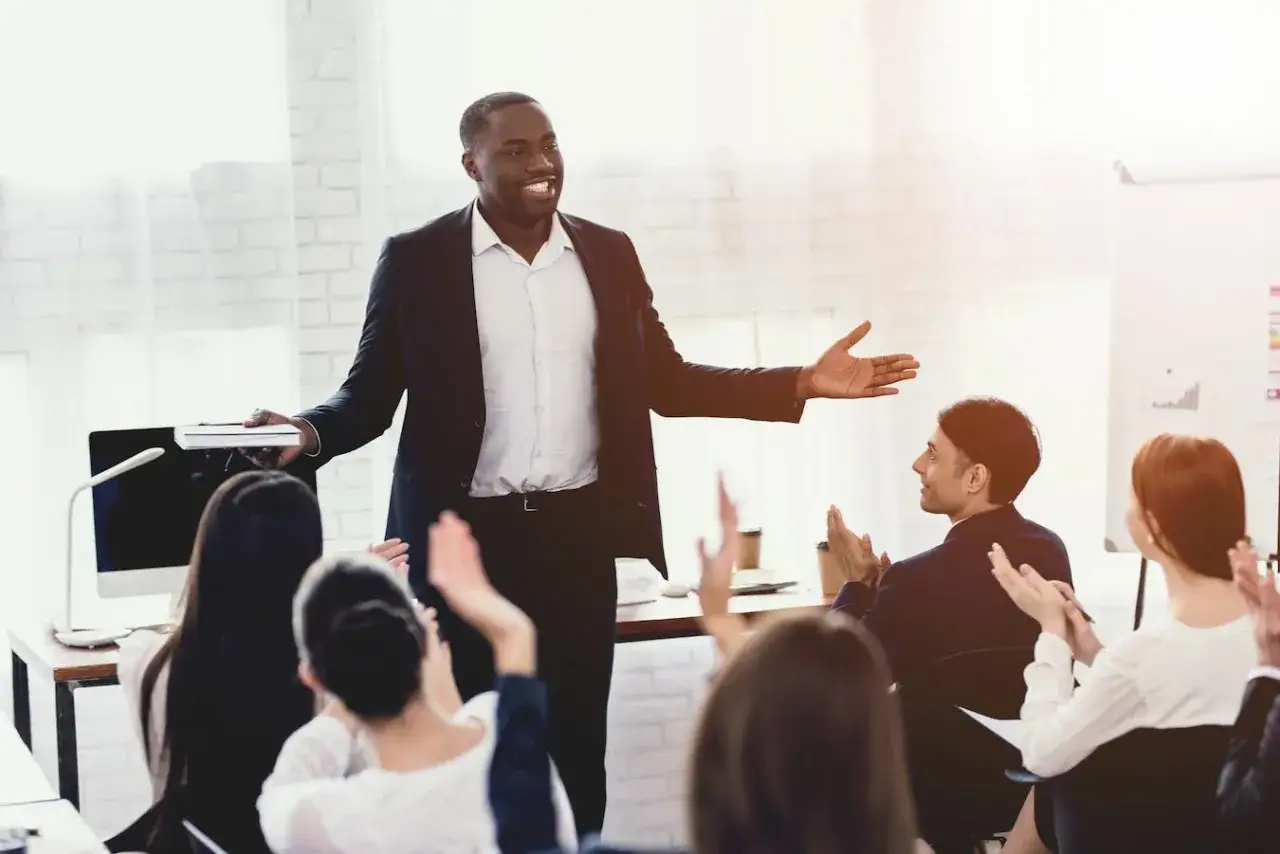 A confident speaker shares public speaking tips with an engaged audience, who applaud his presentation.